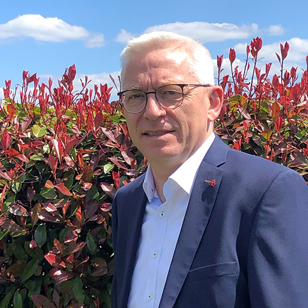 A man in a suit standing in front of bushes.