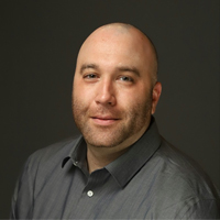 A bald man in a gray shirt is posing for a photo.