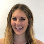A young woman smiling in front of a white wall.