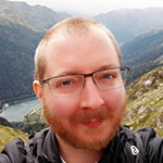 A man with glasses is taking a selfie in front of a mountain.