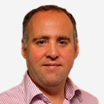 A man in a pink shirt is standing in front of a white background.