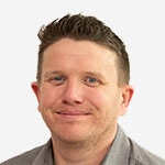 A man in a grey shirt smiling for the camera.