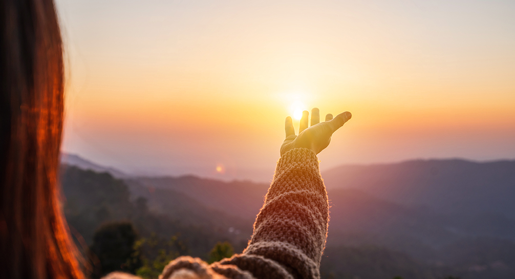 Young woman hand reaching for the mountains during sunset