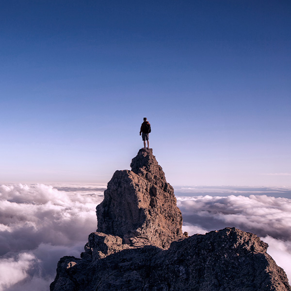 A man standing on top of a mountain overlooking the clouds.
